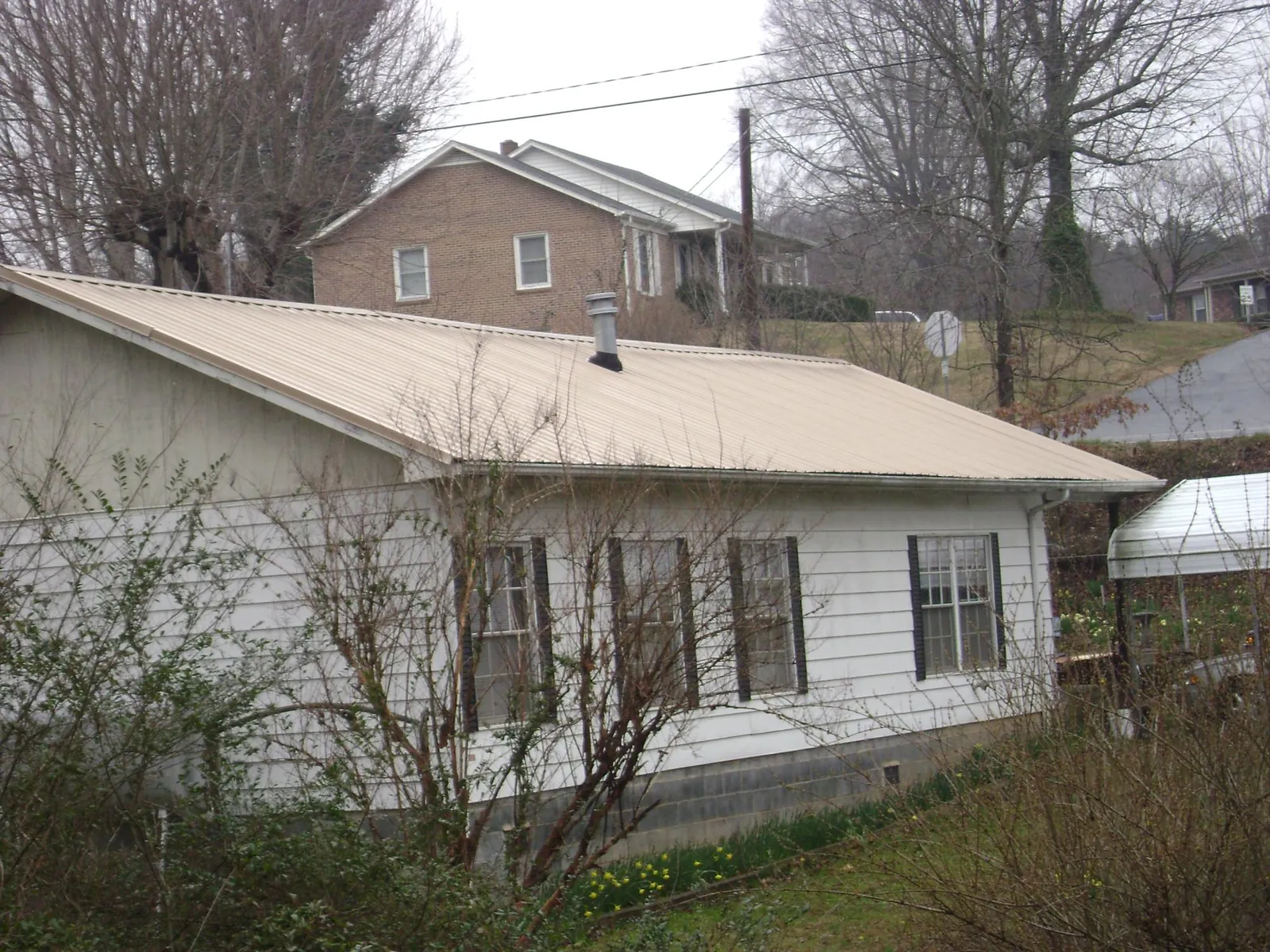 Tan metal roof on a white sided house set into a hillside — Commercial Roofing by Roofing Brothers in Adamstown